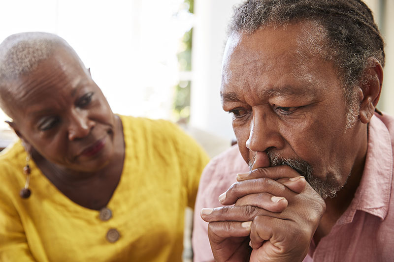 A woman places her hand on her husband's shoulder while he looks down